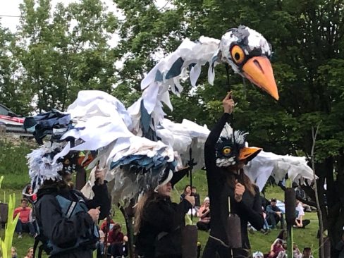 A large bird puppet being held by three people.